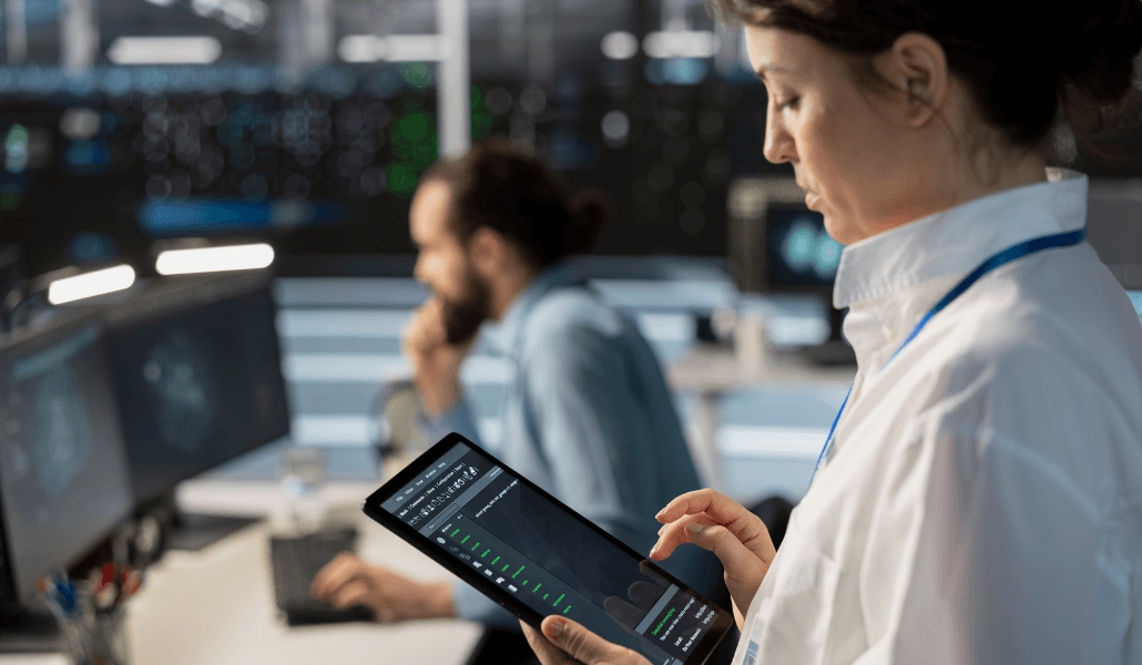 Employee reviewing monitoring software data on a tablet in a control room setting.