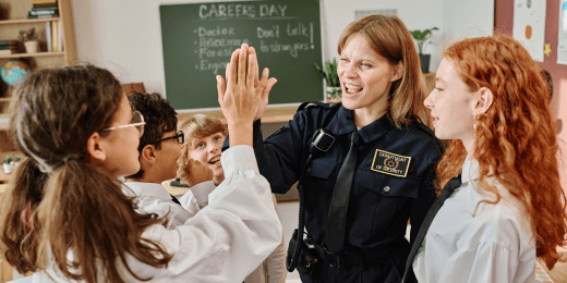 A police officer giving a high five to a bunch of school students.