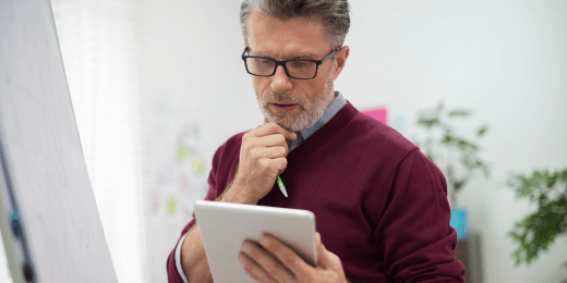 Man in glasses studying a tablet next to a whiteboard.