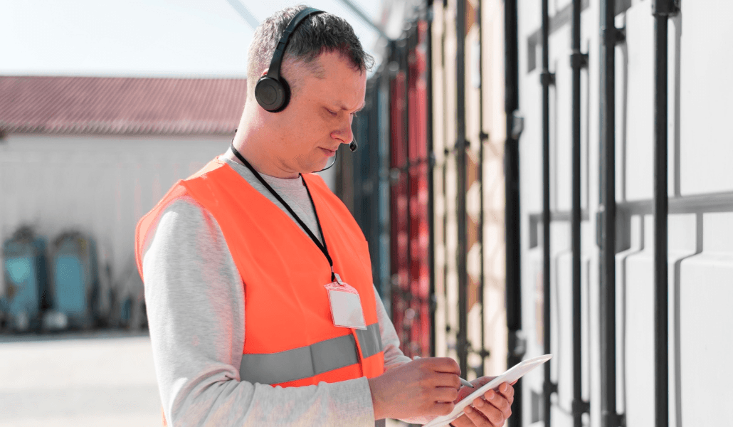 Worker in an orange safety vest checking paperwork next to shipping containers