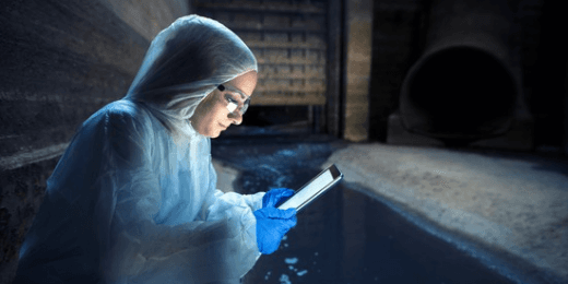 Worker in protective suit, goggles and gloves checking a tablet beside a dark spill