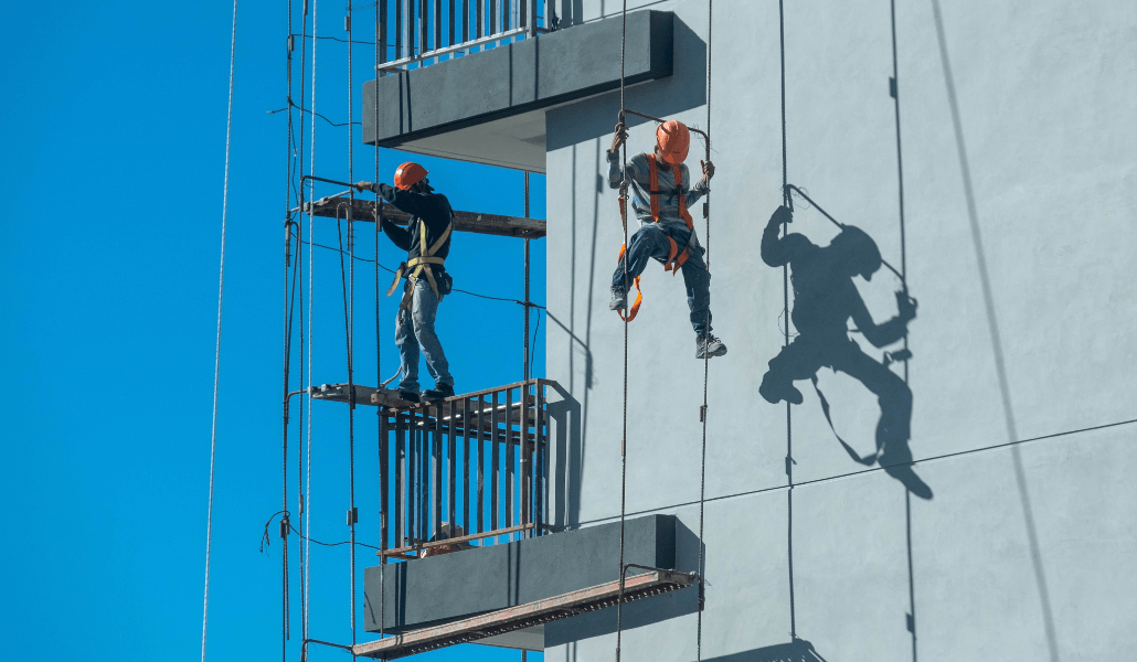 Construction workers using harnesses and rope access to work at height on a building.