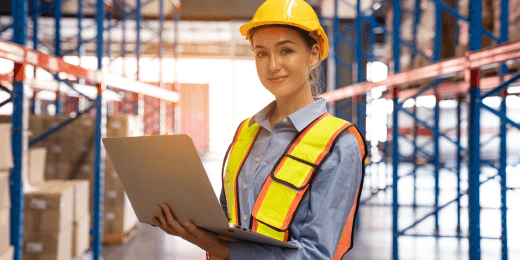 Woman in manufacturing PPE holding a laptop inside a warehouse