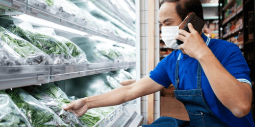 Supermarket worker on the phone while checking a refrigerated produce display