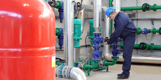 Engineer in protective gear adjusting valves in an industrial facility with pipes, pumps, and a pressure gauge.