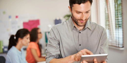 Man in a grey shirt using a tablet while colleagues work behind him